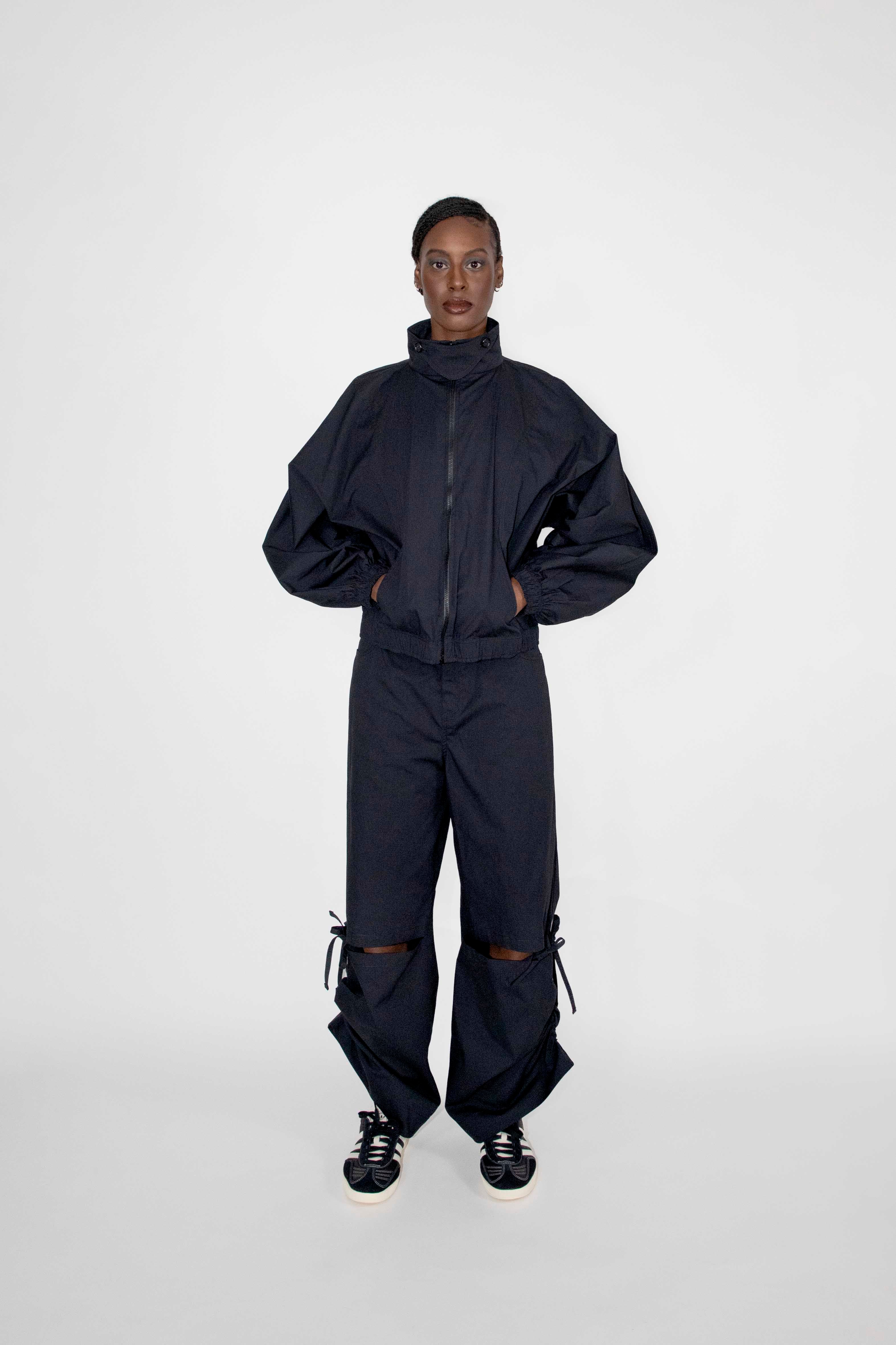 person wearing matching black track jacket and loose pants with black and white sneakers