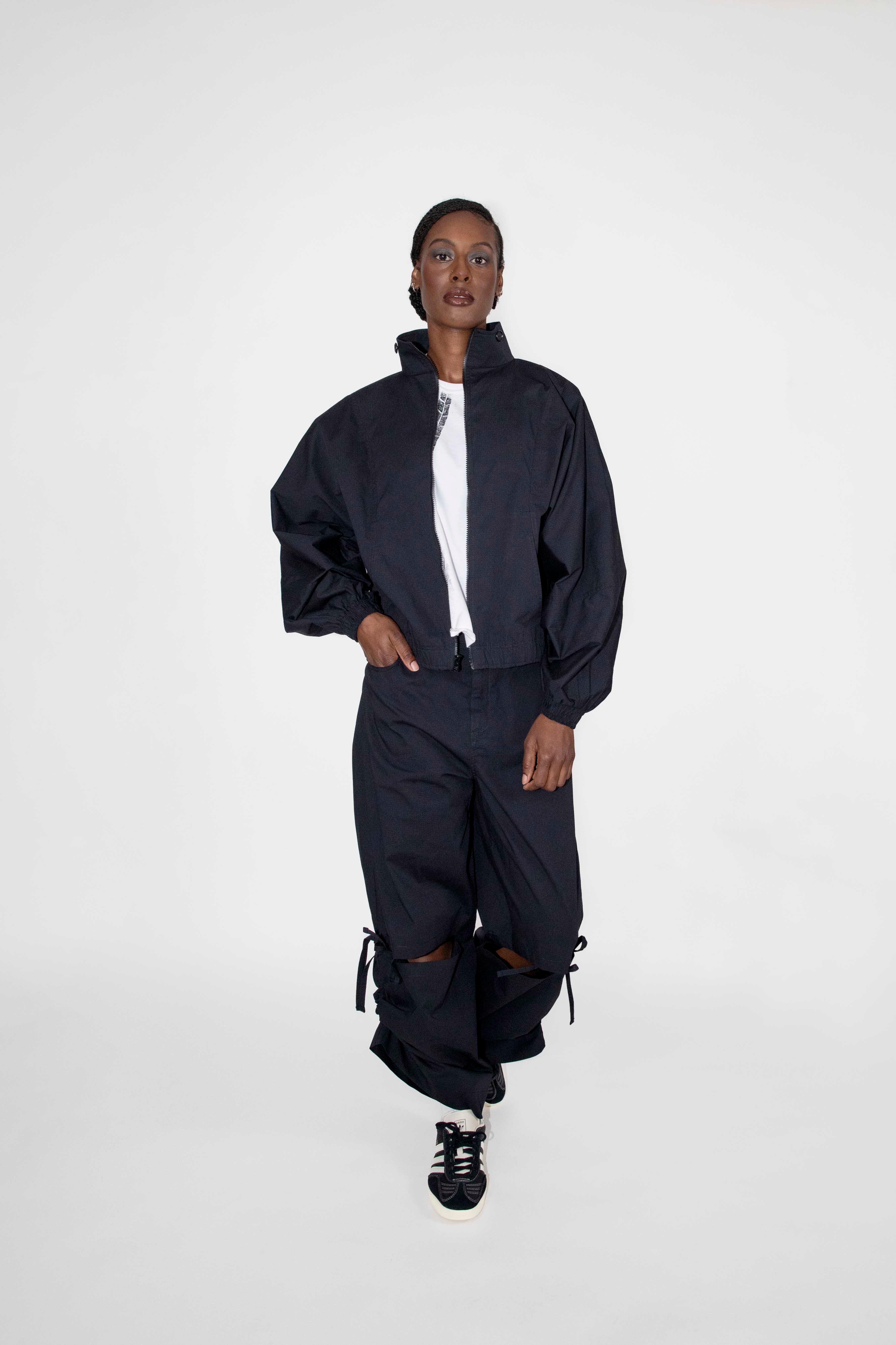 person wearing matching black track jacket and loose pants with black and white sneakers and a white t-shirt underneath