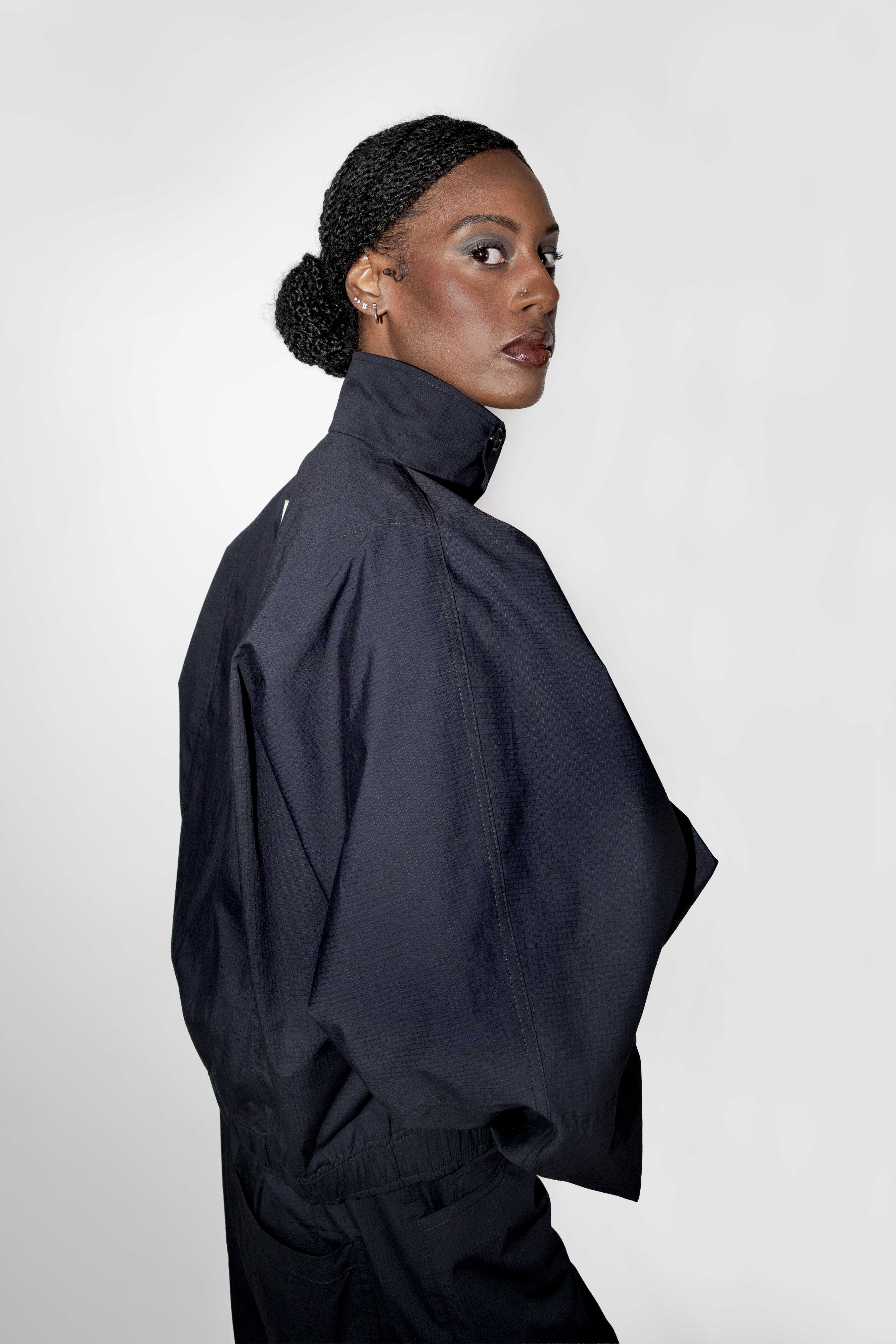 person wearing a black track jacket with matching pants shown from a side back angel