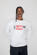 A model wearing a white long-sleeve sweatshirt with a 'I LOVE NY' graphic on the chest, paired with black pants, against a plain light gray background.