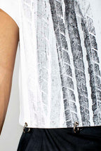 Close-up of a sleeveless white top with a vertical black and gray textured graphic print, worn by a model with black pants.
