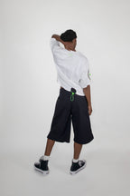 Person wearing a white shirt and black shorts with green accents on a white background