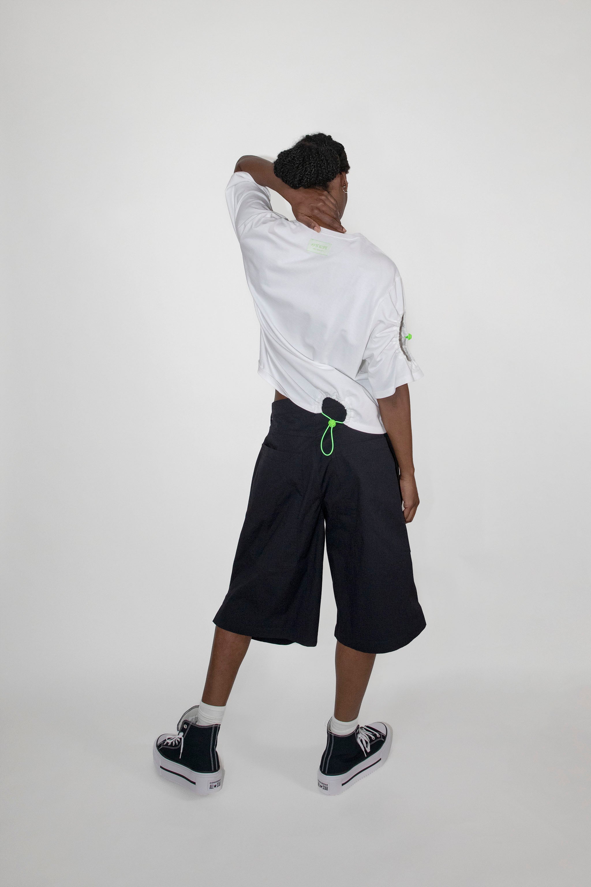 Person wearing a white shirt and black shorts with green accents on a white background