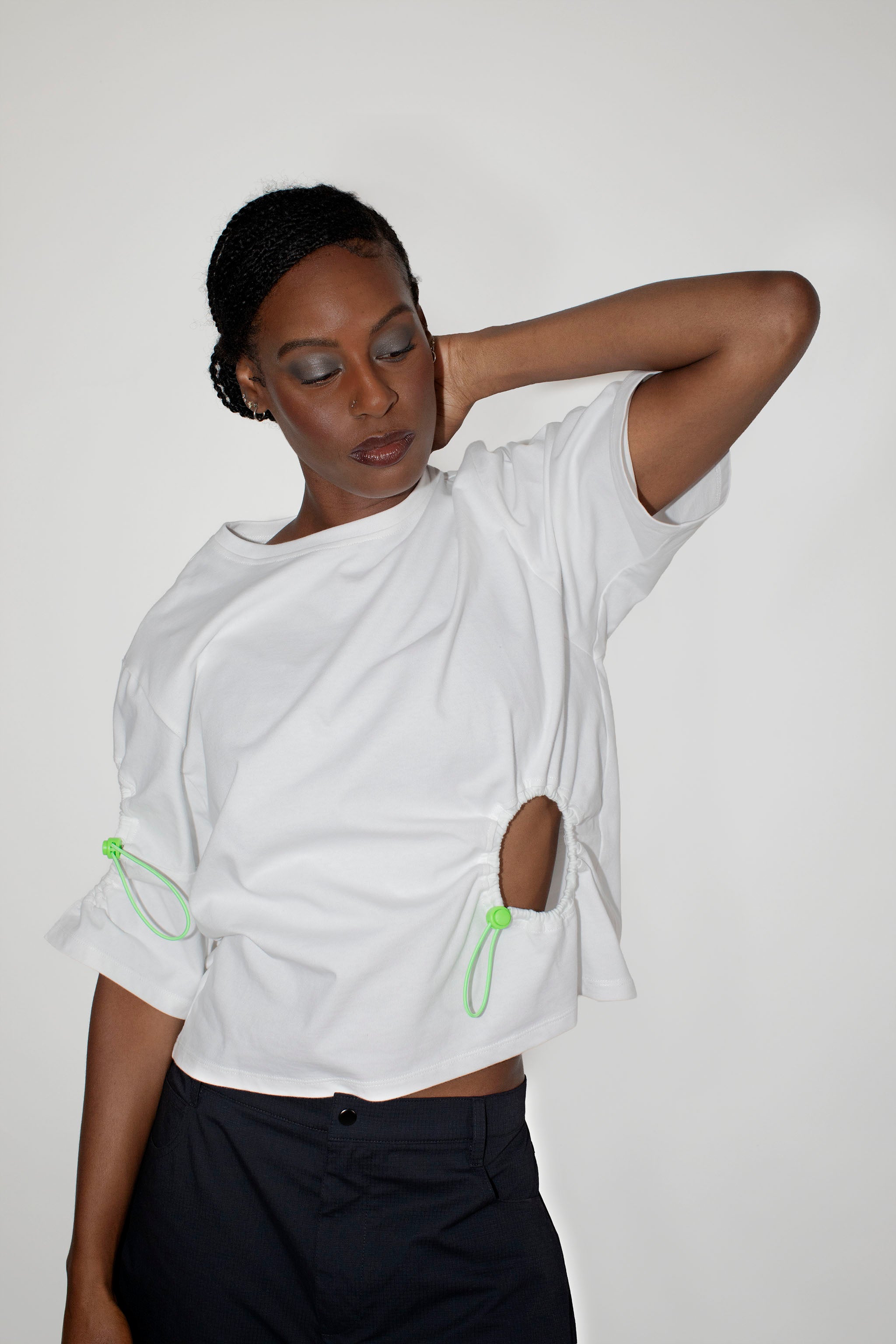 Person wearing a white t-shirt with green accents and black shorts on a plain background