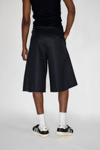 Person wearing black shorts, black tank top, white socks, and Adidas shoes on a white background