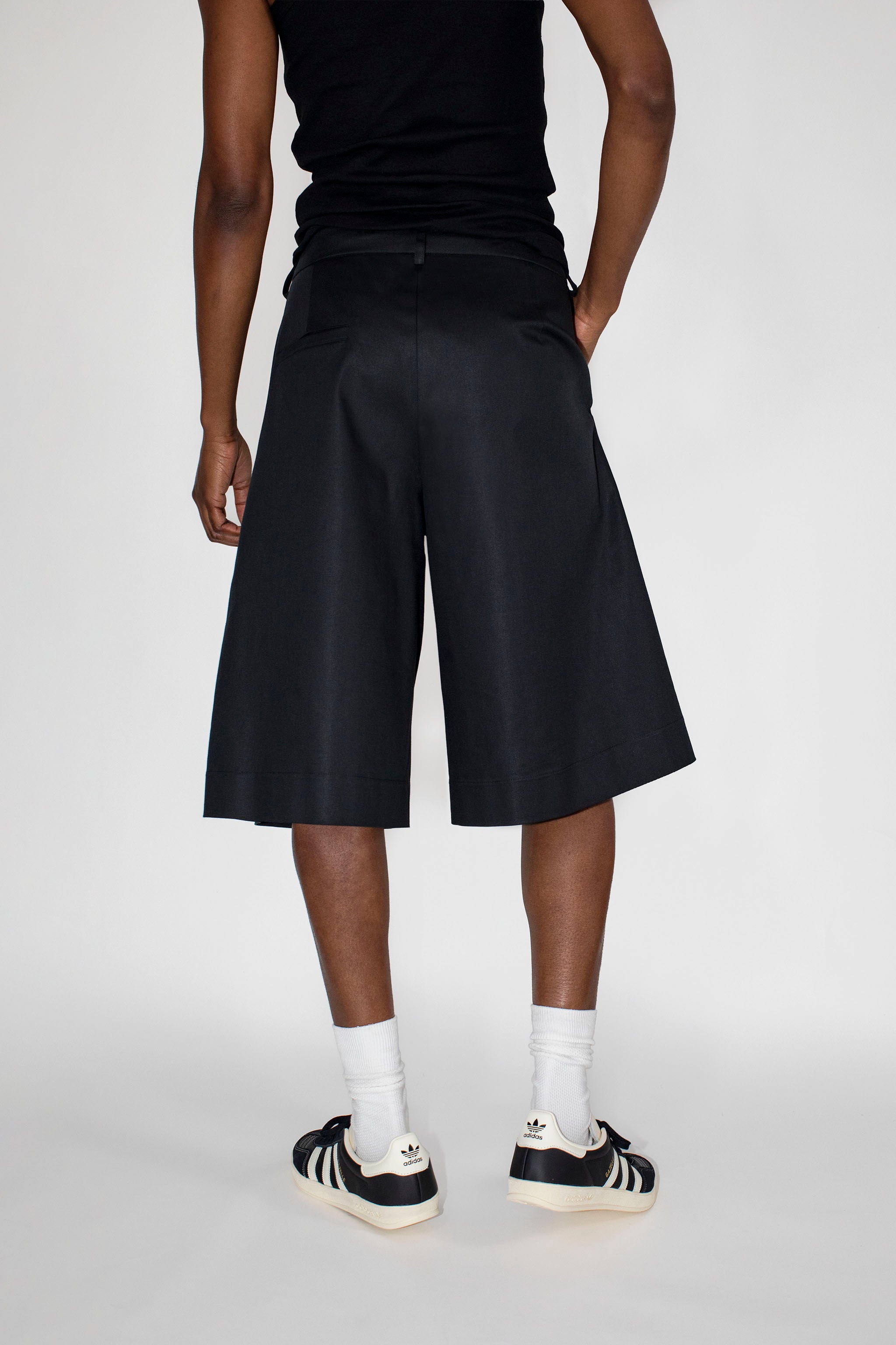 Person wearing black shorts, black tank top, white socks, and Adidas shoes on a white background