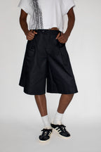 Person wearing black dress shorts, white shirt, and black and white sneakers on a plain background
