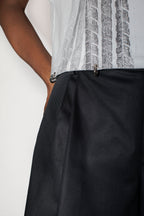 Person wearing a white top with black pattern and black dress shorts on a white background