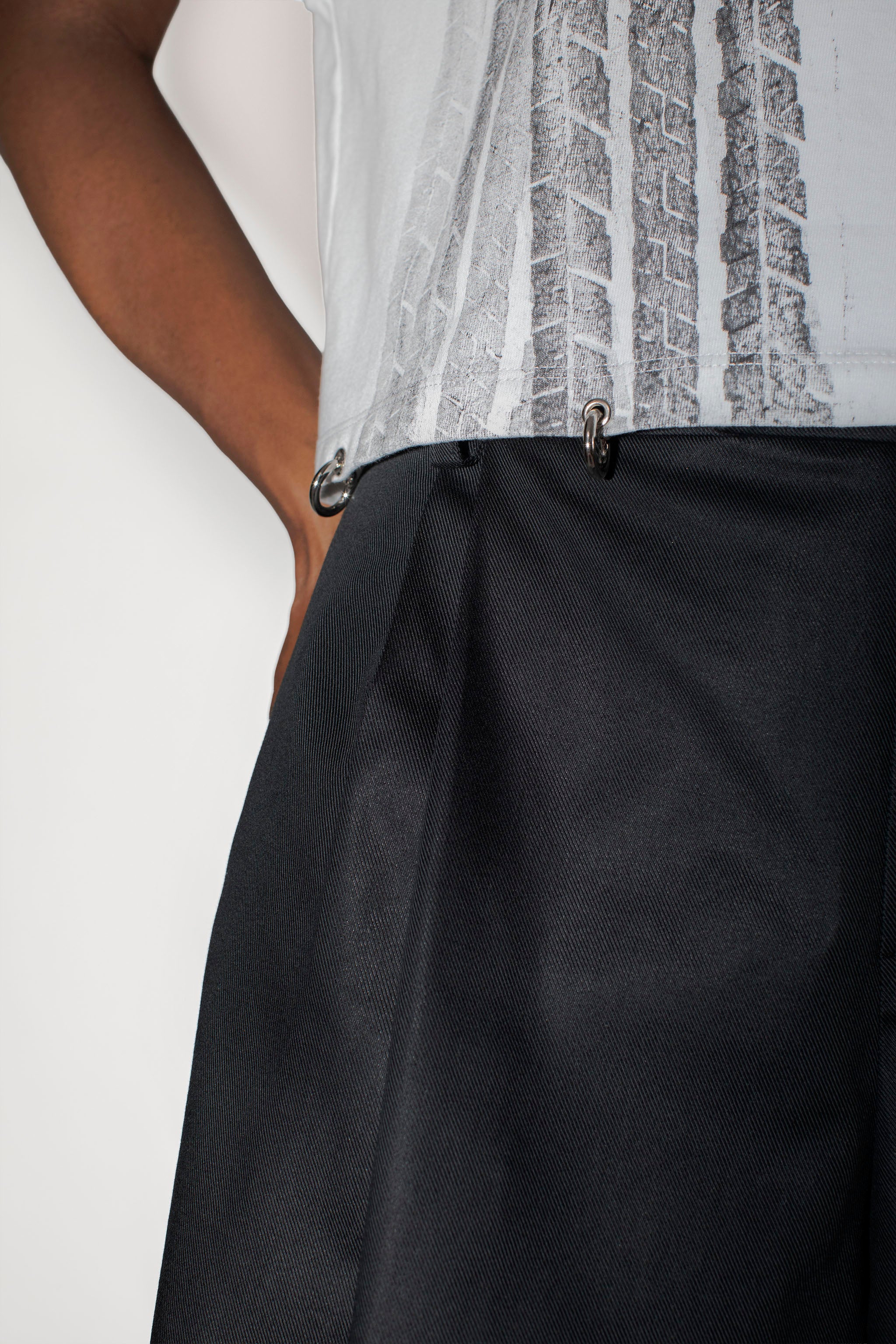 Person wearing a white top with black pattern and black dress shorts on a white background