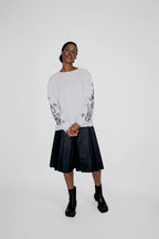 Person wearing a white longsleeve with black floral and flames patterns and a black skort on a white background