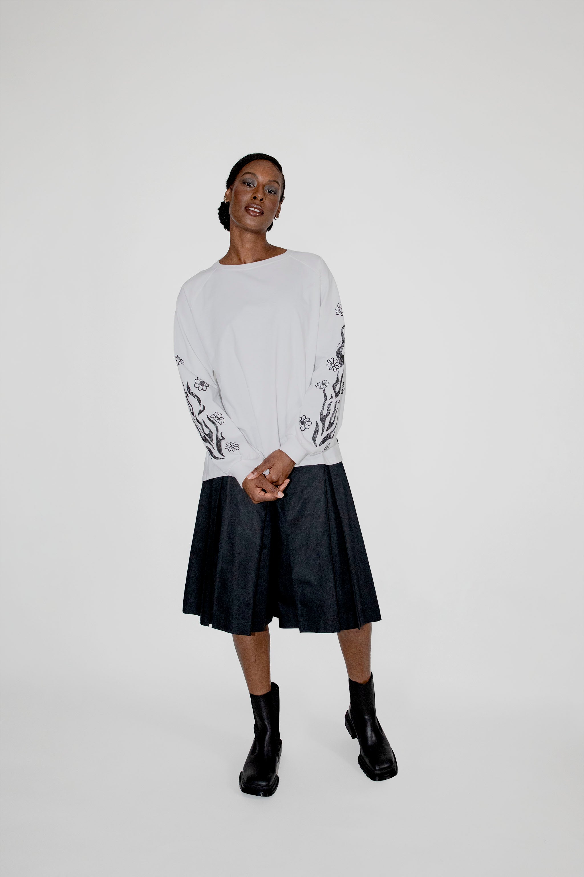 Person wearing a white longsleeve with black floral and flames patterns and a black skort on a white background