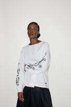 Person wearing a white long-sleeve top with black floral and flames print on a plain background