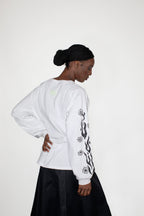 Person wearing a white longsleeve with black floral and flames print on a plain background