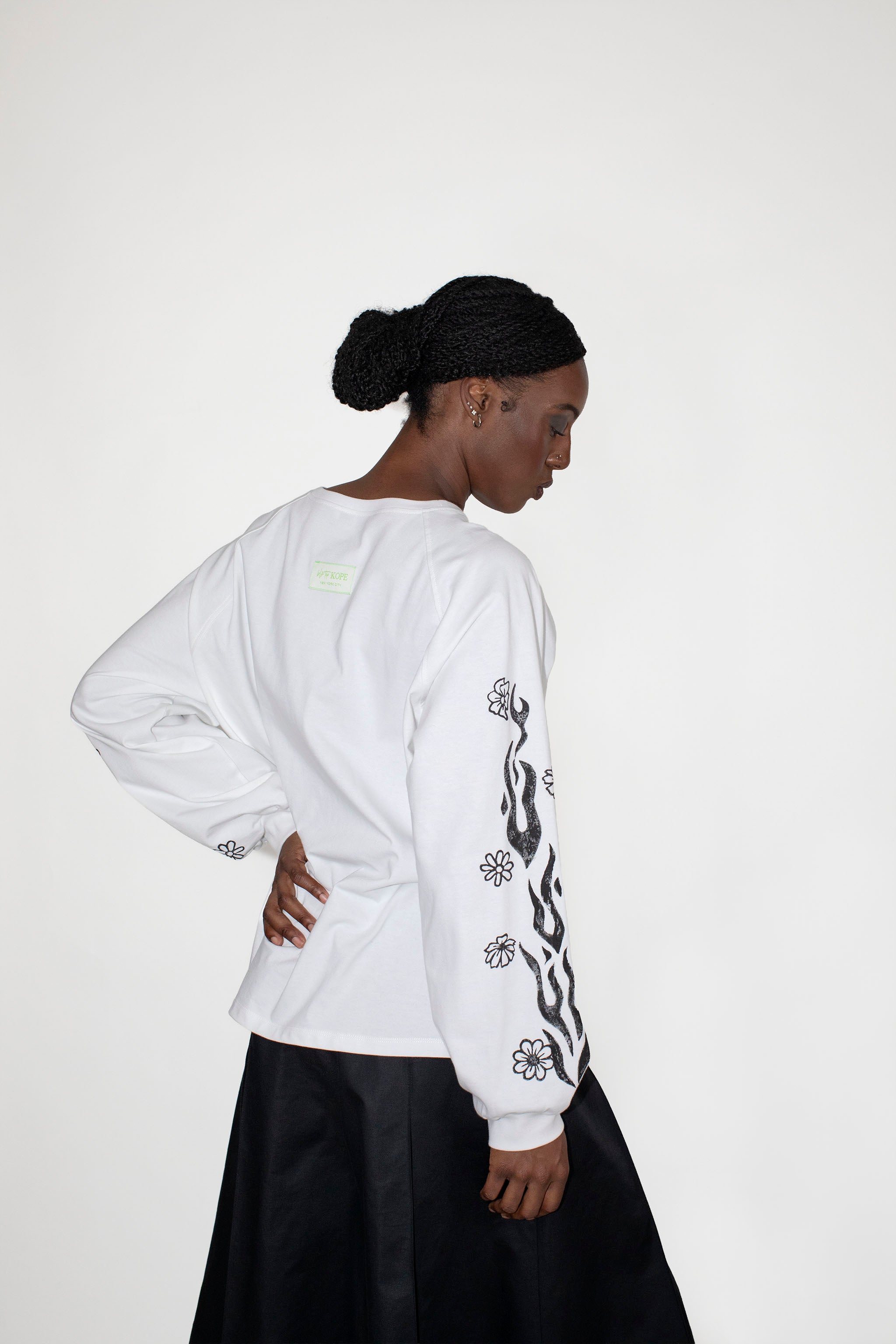 Person wearing a white longsleeve with black floral and flames print on a plain background