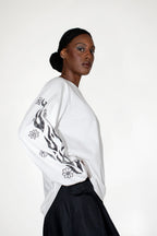 Woman wearing a white longsleeve with black floral and flames print on a plain background