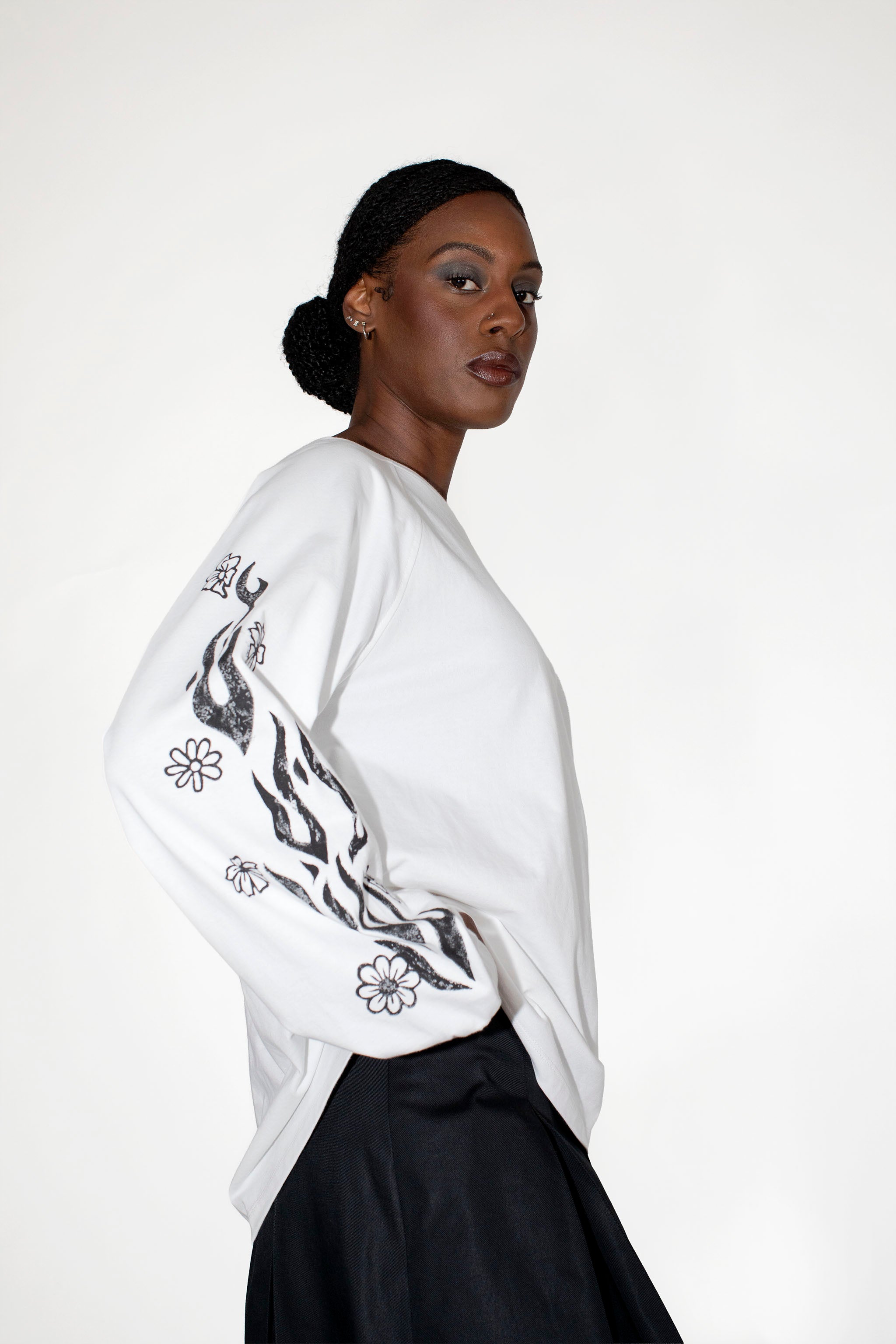 Woman wearing a white longsleeve with black floral and flames print on a plain background