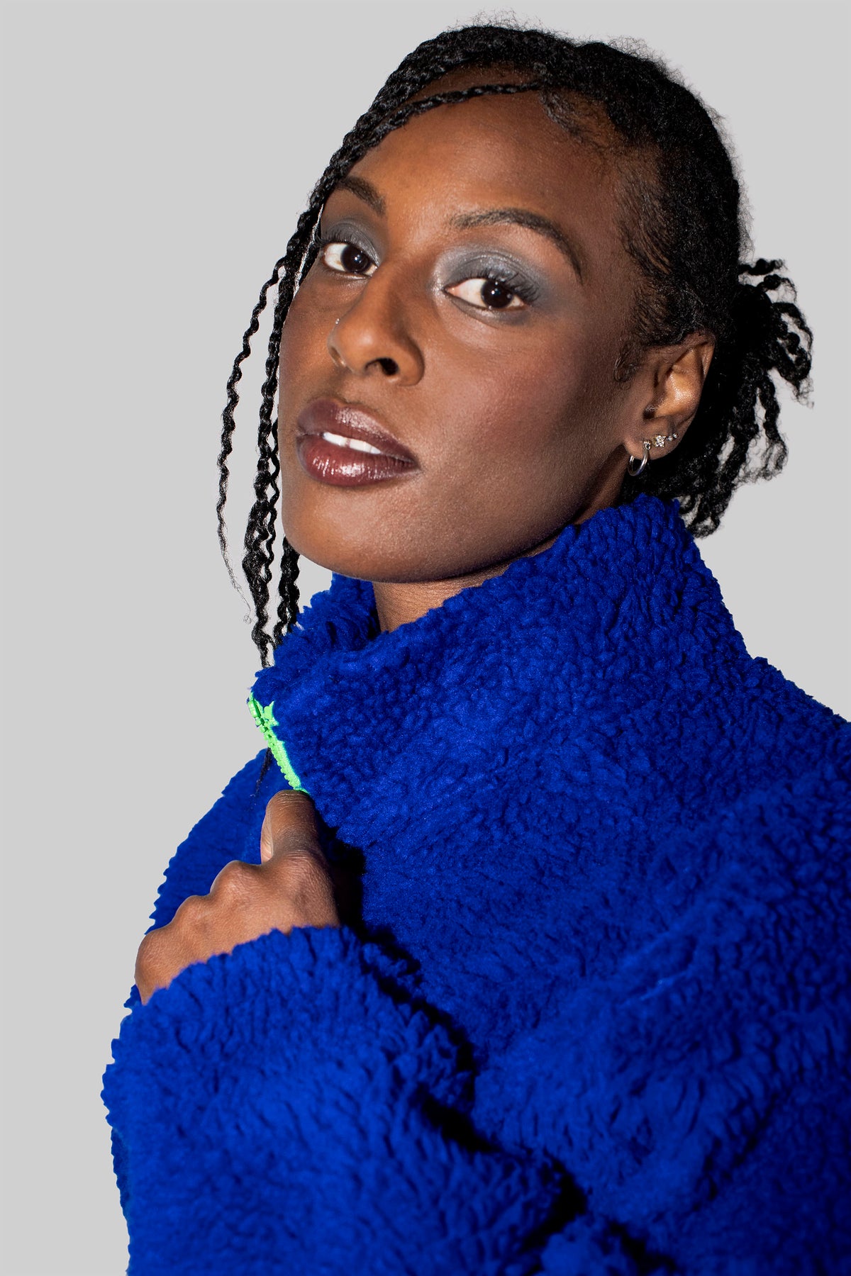 A close-up portrait of a woman wearing a vibrant royal blue fuzzy fleece jacket against a solid light gray background.