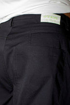 Close-up of the back waistband and pocket area of dark charcoal pants, with a white shirt hem visible at the top and a small light label reading blk top KOPE.