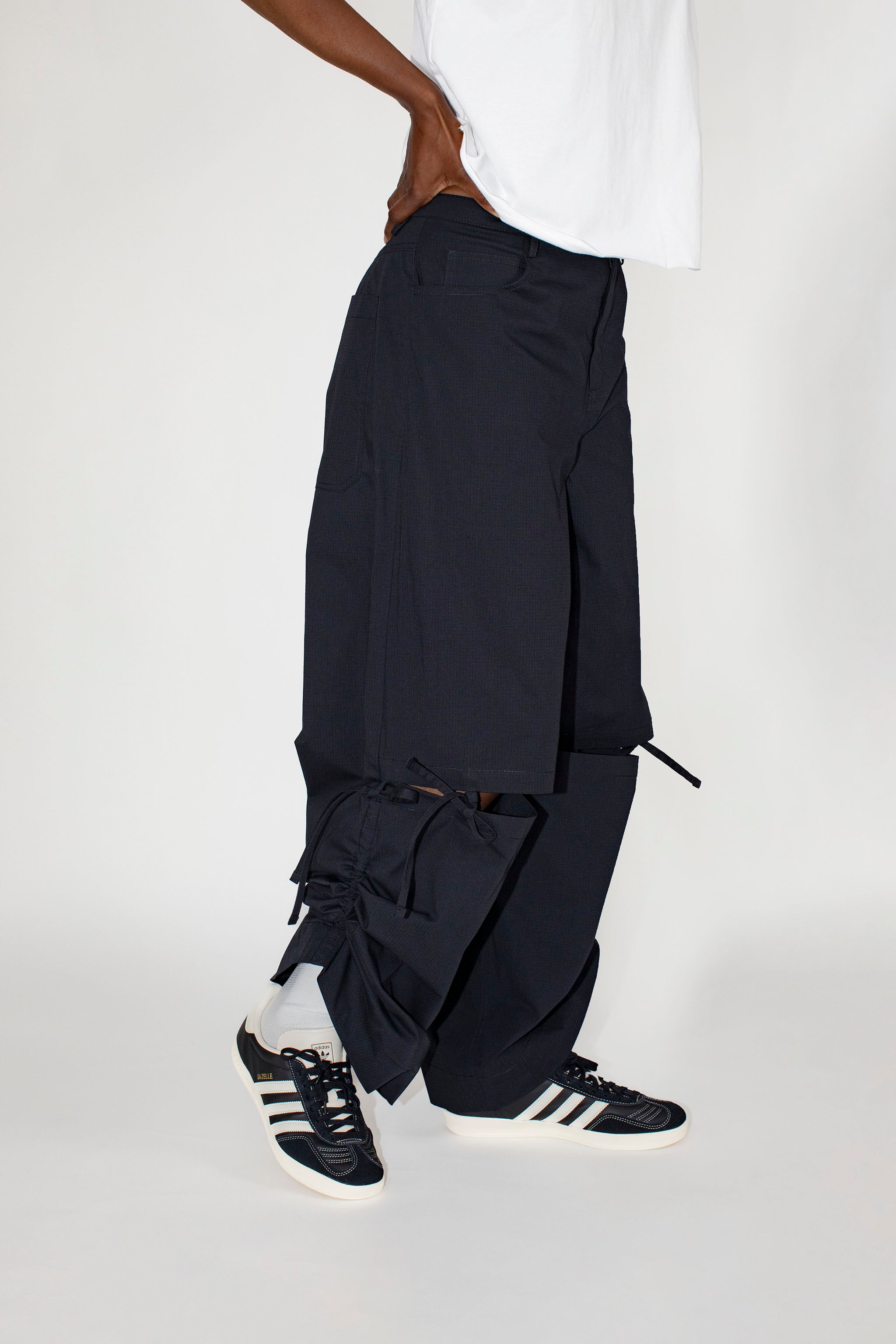 Person wearing black pants and black sneakers with white stripes on a white background