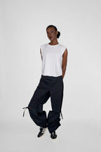person wearing white sleeveless top and black loose pants with black and white sneakers