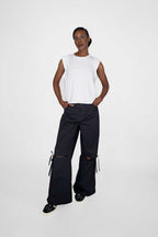 person wearing white sleeveless top and black loose pants with black and white sneakers