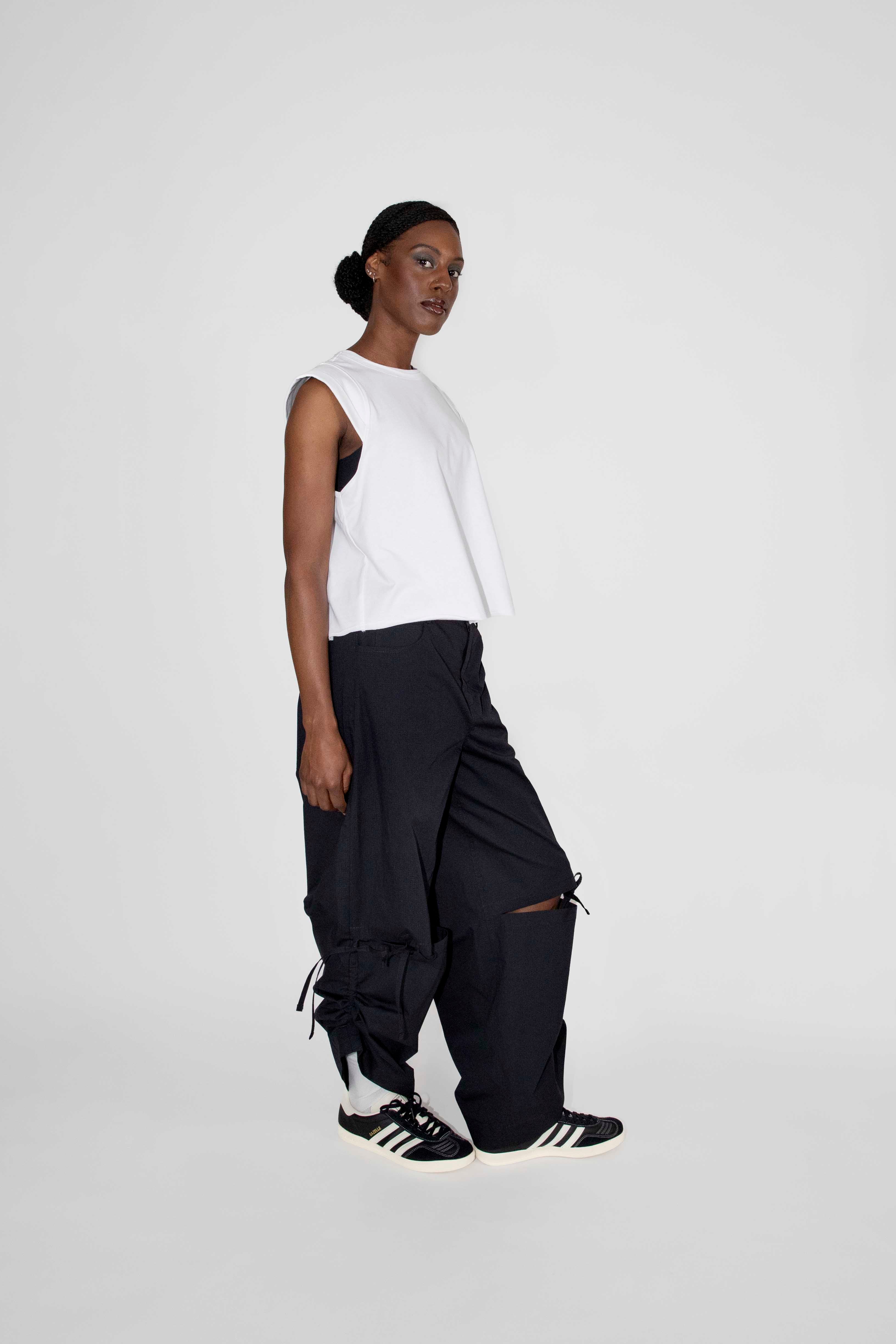 person wearing white sleeveless top and black loose pants with black and white sneakers