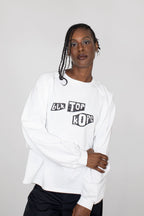 A model wearing a white long-sleeve sweatshirt with a black graphic text print reading 'BLK TOP KOPE' on the chest, paired with black pants, against a light gray studio background.