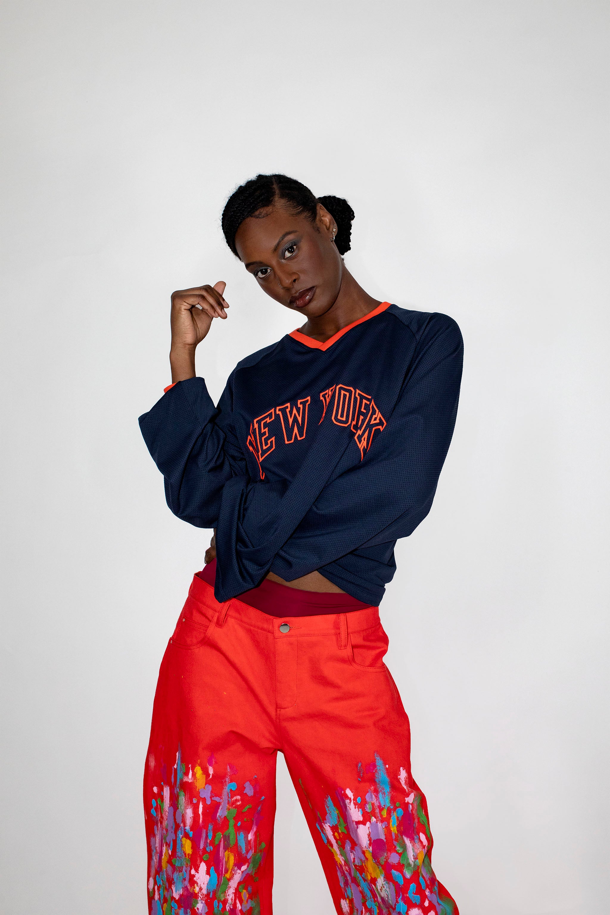Person wearing a navy 'New York' sweatshirt and red pants with paint patterns on a white background