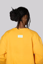 A person shown from the back wearing a yellow sweatshirt against a solid light gray background.