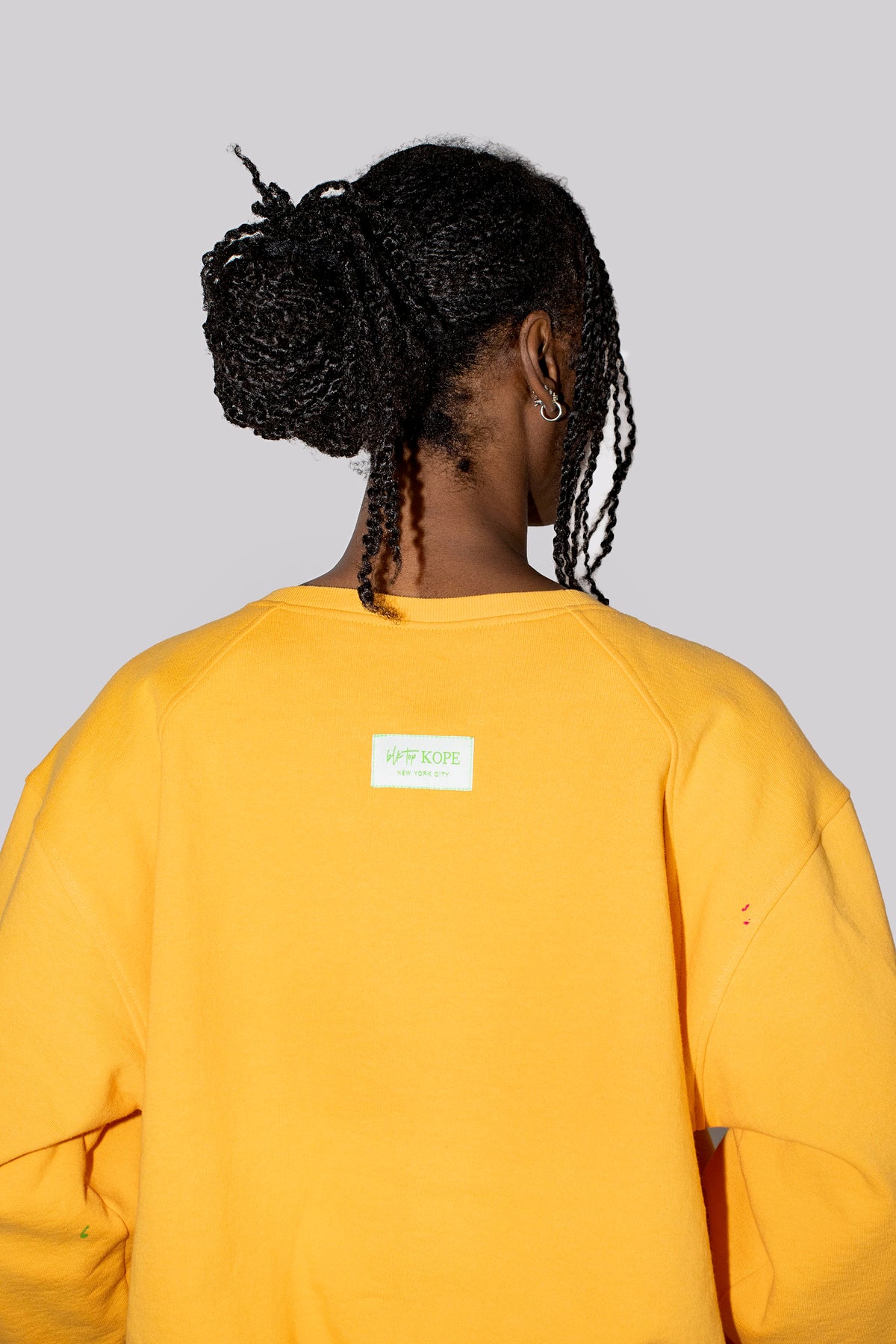 A person shown from the back wearing a yellow sweatshirt against a solid light gray background.