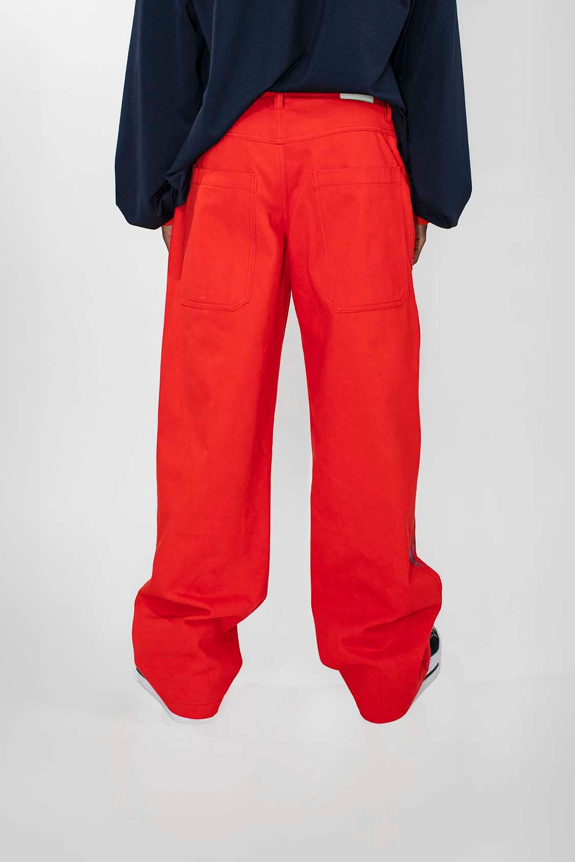 A person shown from the back wearing bright red wide-leg trousers and a dark navy long-sleeve top against a plain light gray studio background.