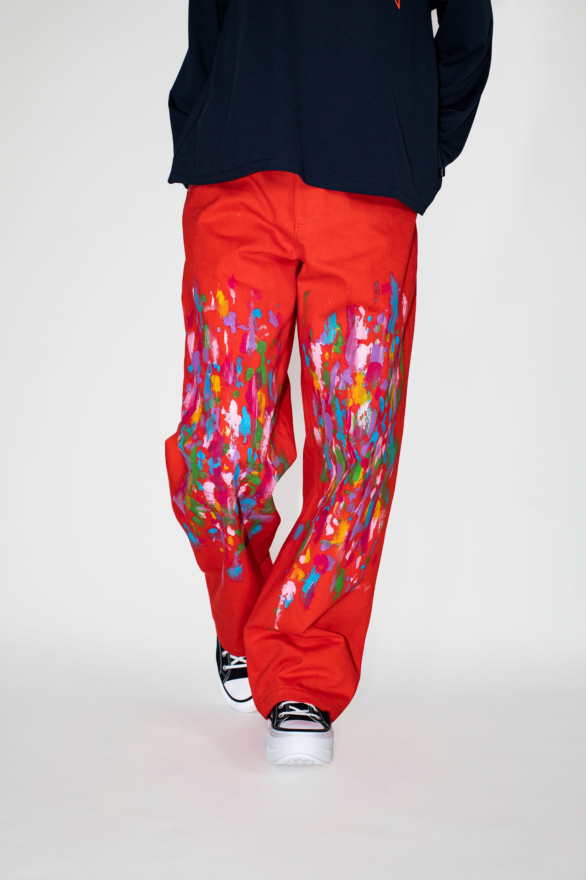 Person wearing red pants with colorful paint patterns and a navy sweatshirt on a white background