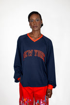 Person wearing a navy blue sweatshirt with 'New York' in red pants with colorful patterns on a white background
