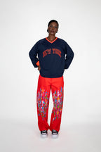 Person wearing a navy sweatshirt with 'New York' text and red pants with colorful paint on a white background
