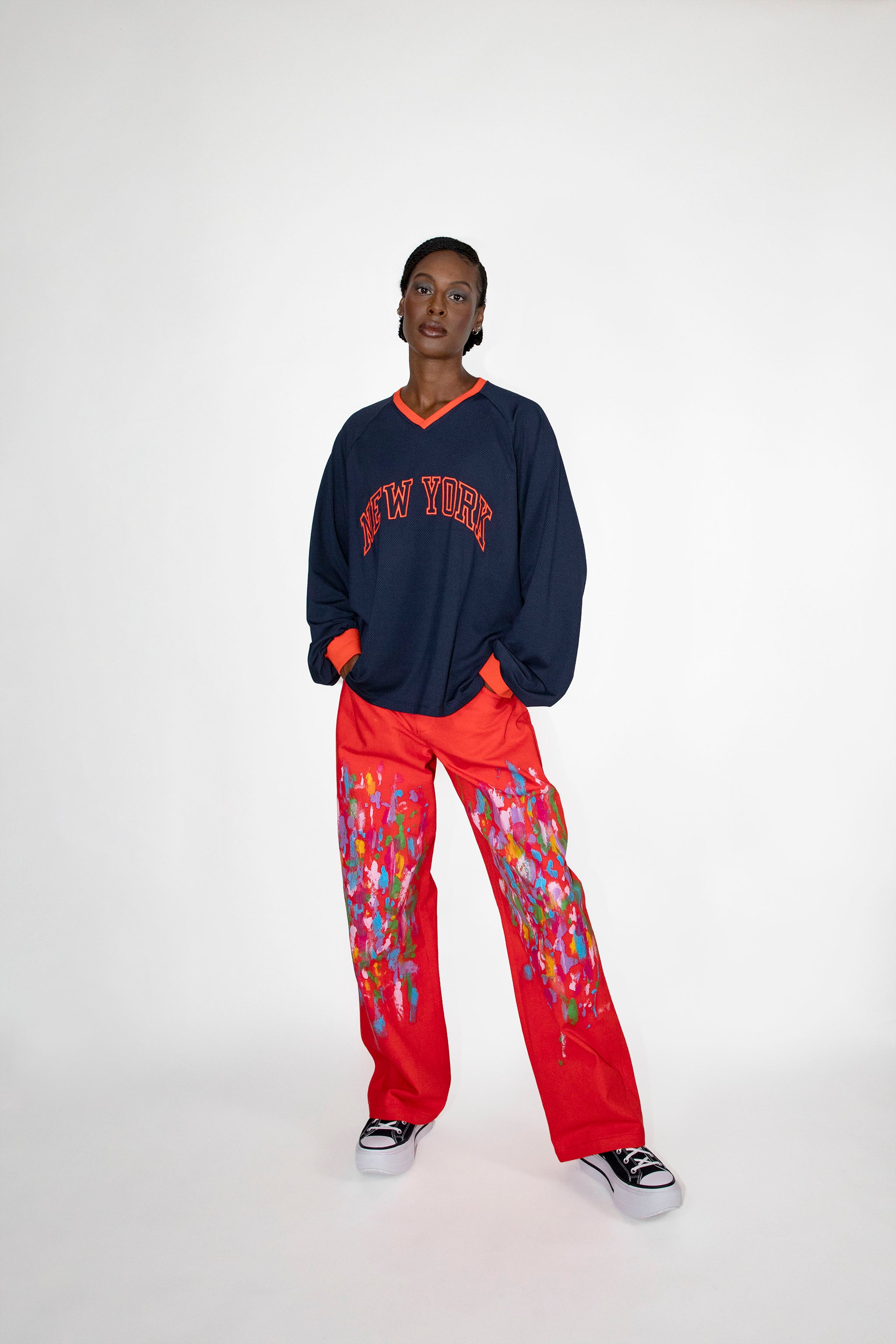 Person wearing a navy 'New York' sweatshirt and red pants with colorful patterns on a white background.