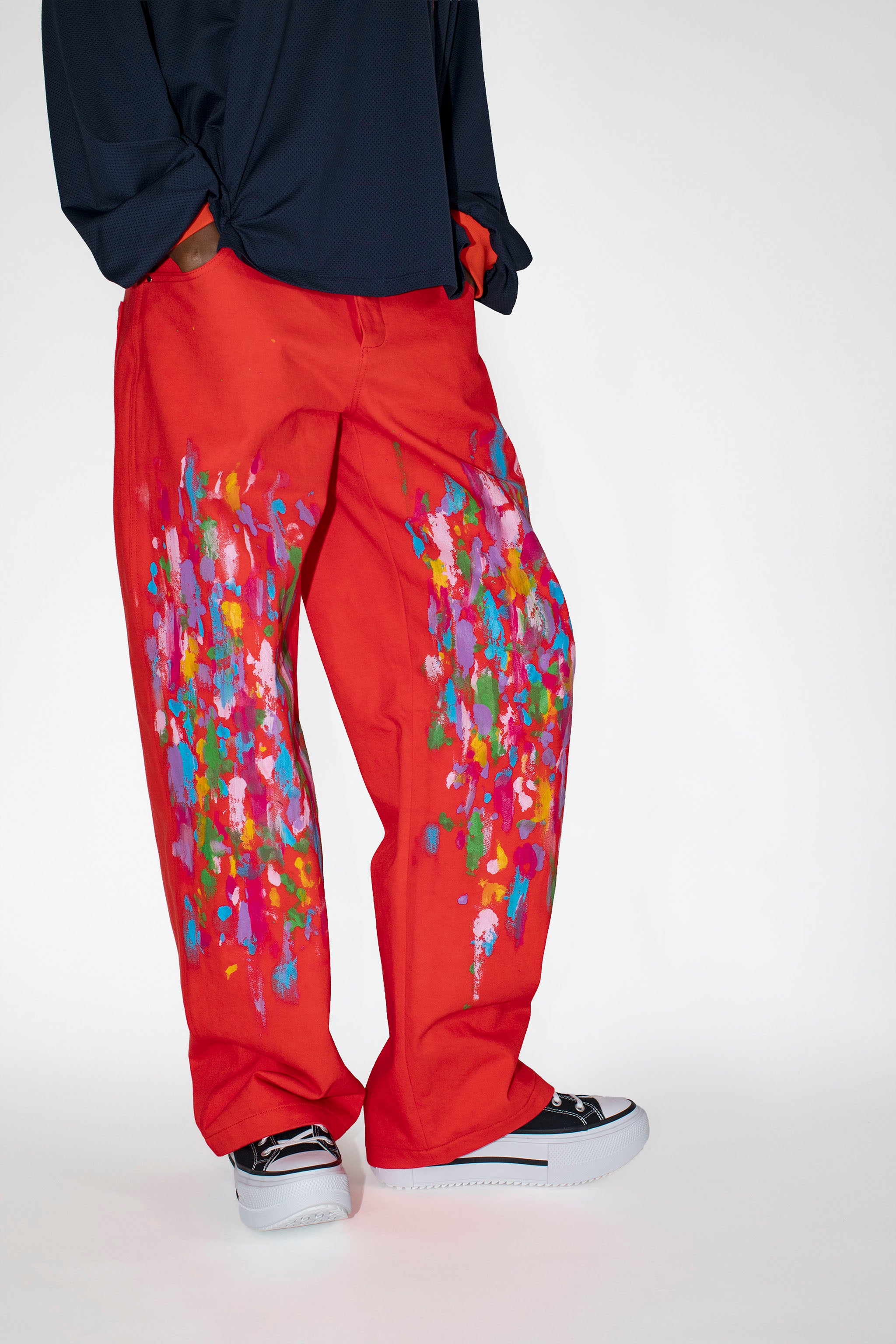 Red pants with colorful abstract paint patterns worn by a person on a white background