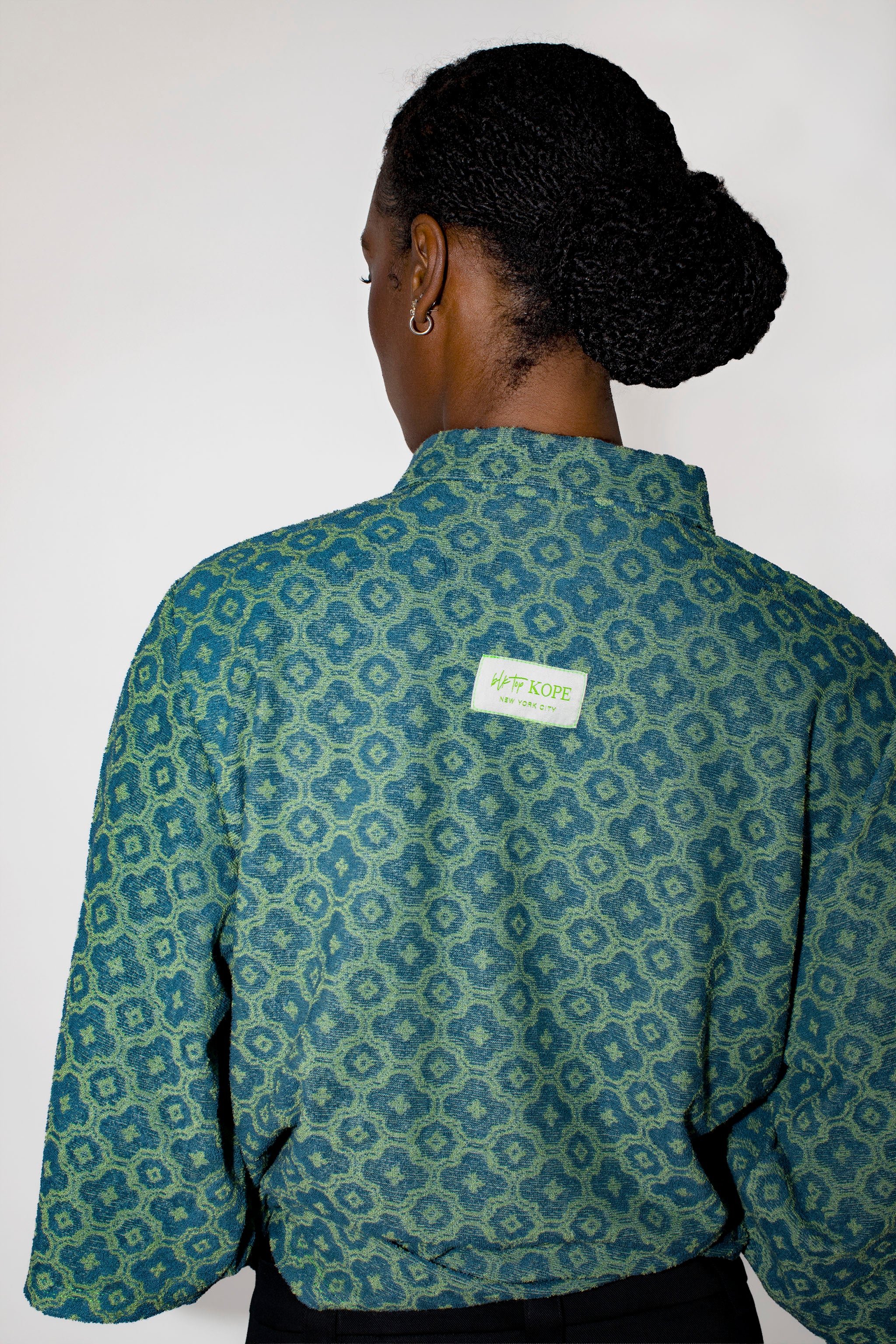 Person wearing a green patterned polo tee with a visible brand label on a white background