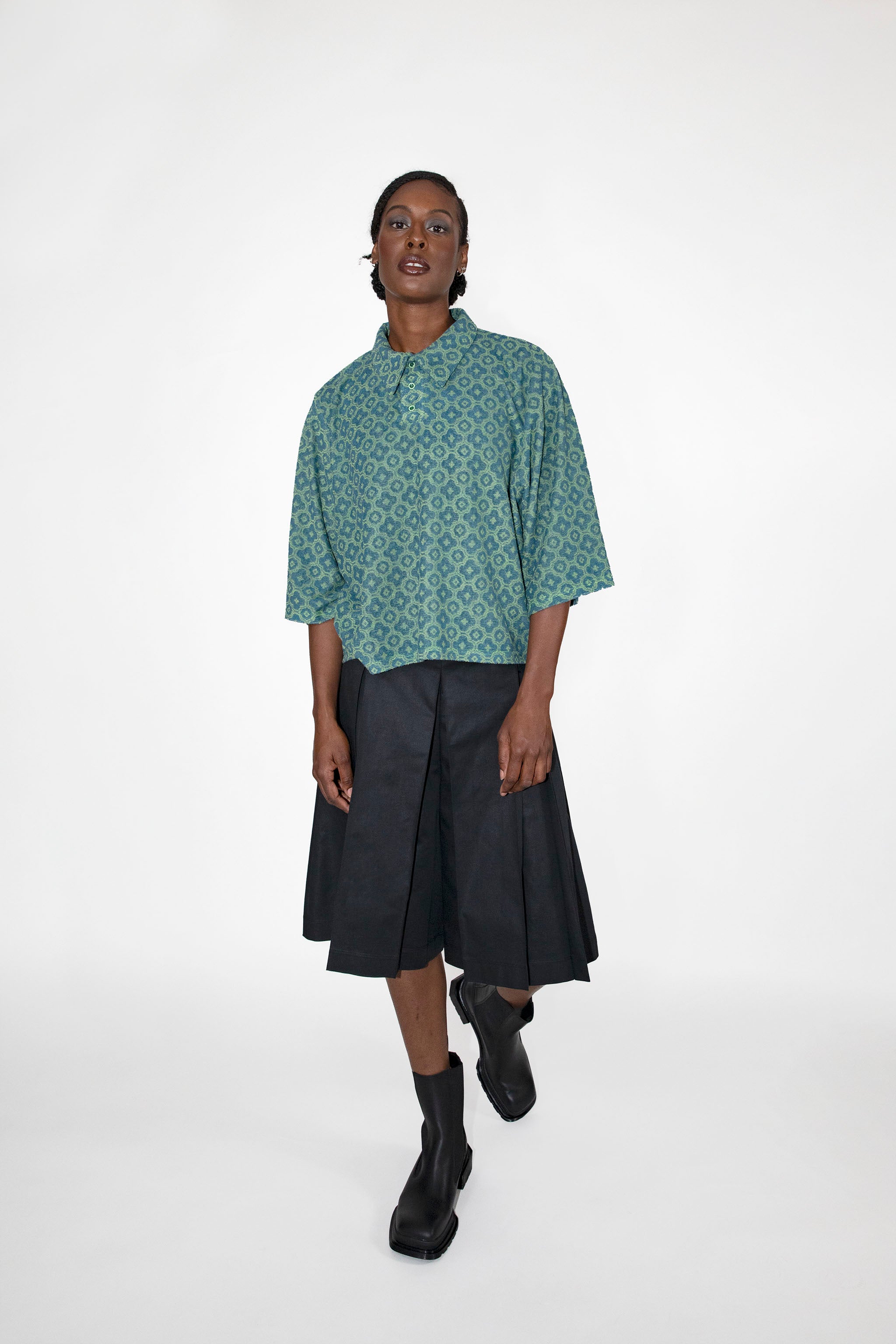Person wearing a green patterned polo shirt and black skort on a white background