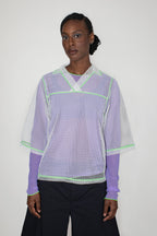 Person wearing a light purple longsleeve with a white mesh t-shirt with green accents on a white background