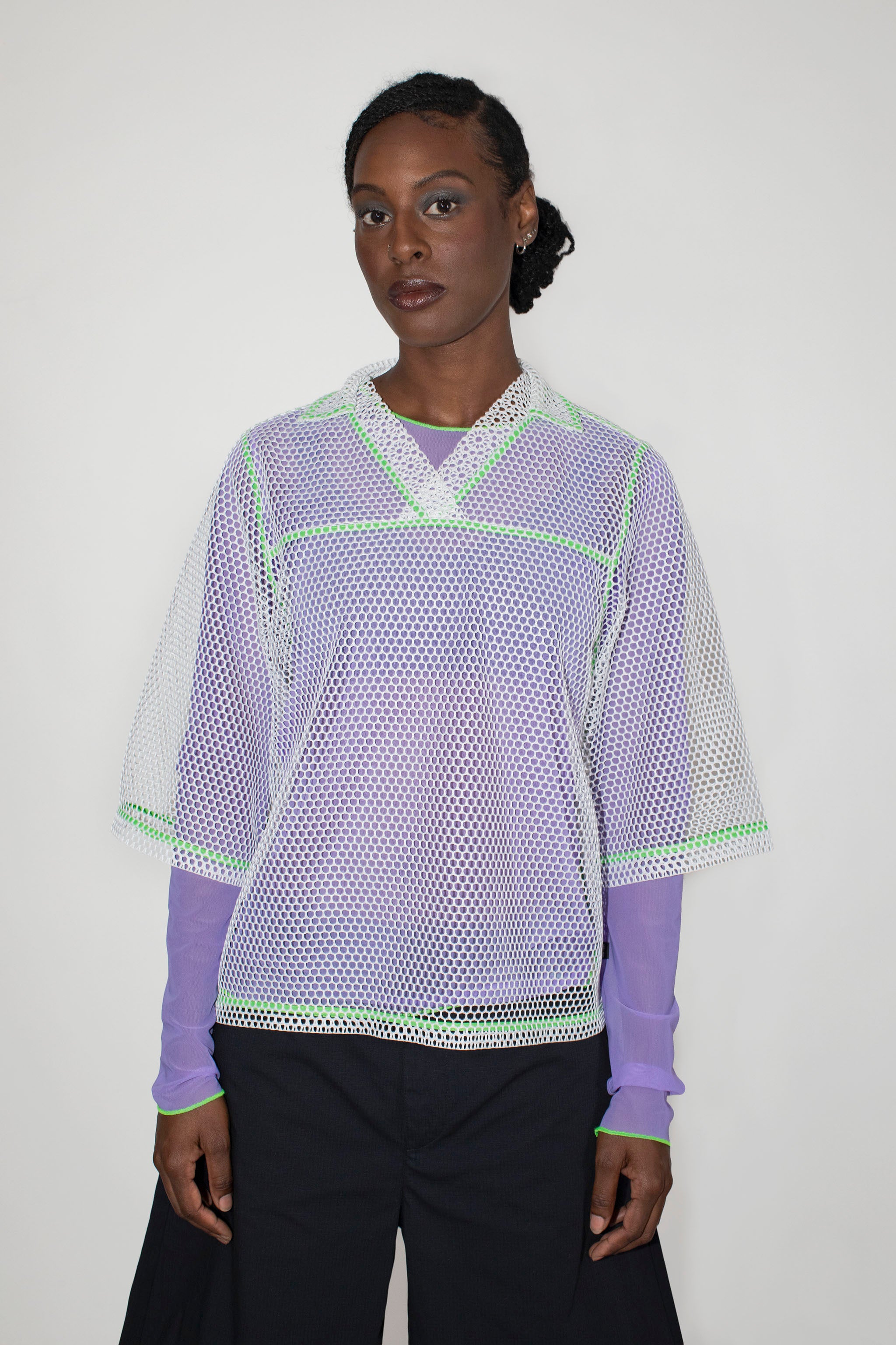Person wearing a light purple longsleeve with a white mesh t-shirt with green accents on a white background
