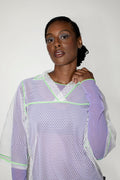 Woman wearing a light purple and white mesh top against a plain background