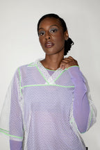 Woman wearing a light purple and white mesh top against a plain background