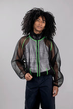 A model with curly black hair wearing a black mesh jacket with bright green piping, paired with dark trousers, against a solid light gray background.