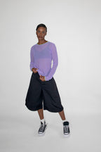 Person wearing a light purple long-sleeve top and black shorts on a white background