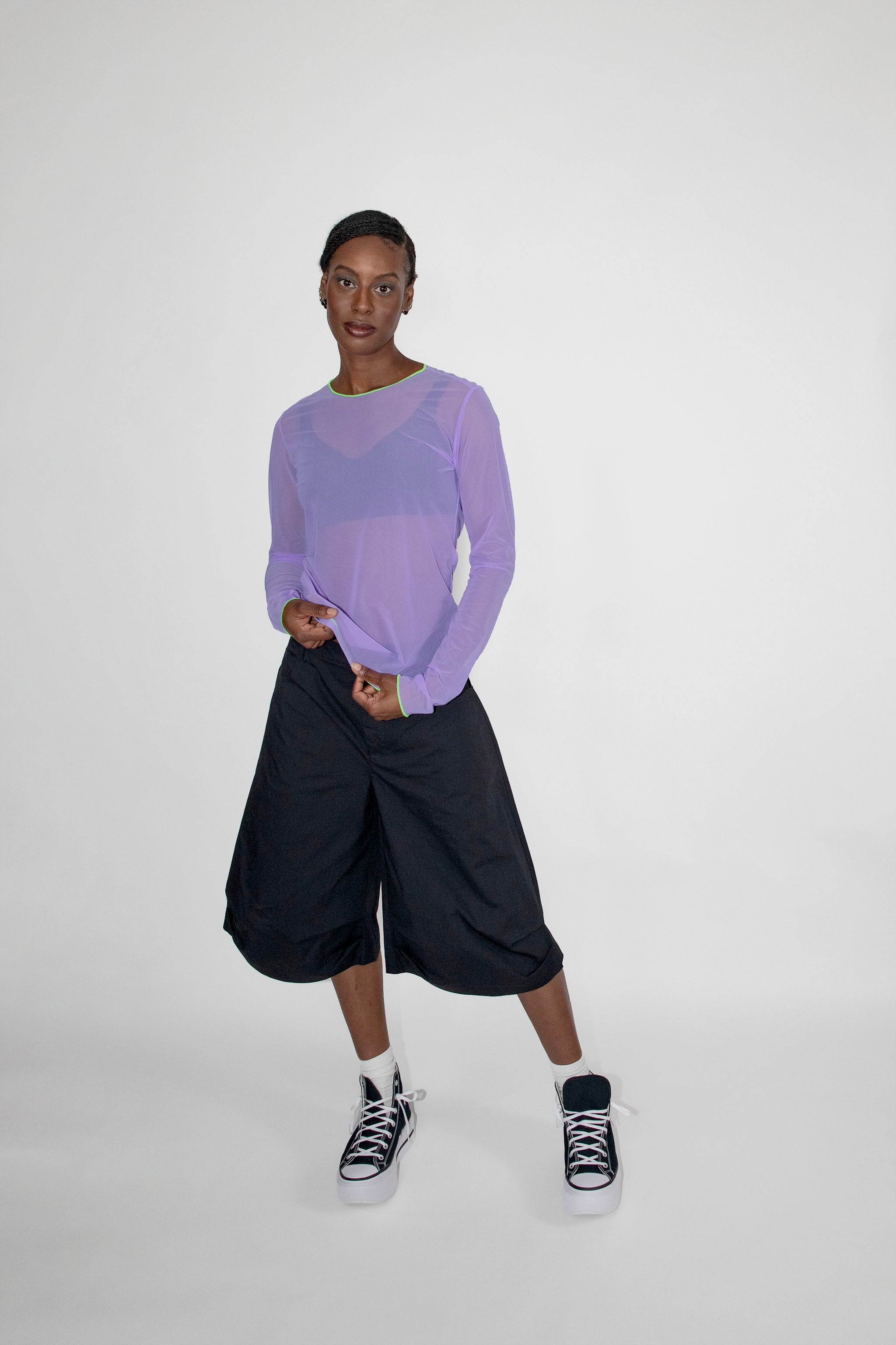 Person wearing a light purple long-sleeve top and black shorts on a white background