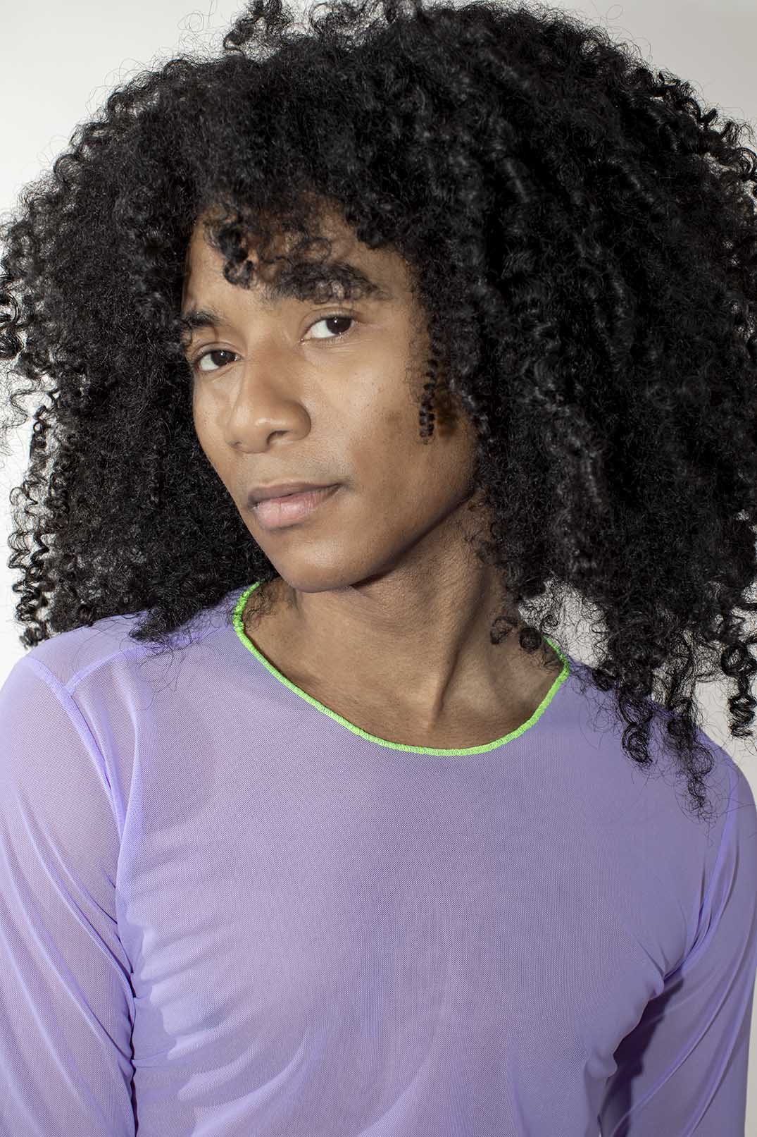 person with voluminous black curly hair wearing a sheer lavender mesh longsleeve