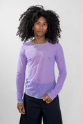 A model with curly black hair wearing a light purple sheer long-sleeve shirt with a thin lime green collar and cuffs, paired with black pants, against a light gray background.