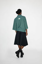 Person wearing a green patterned polo shirt and black skort on a white background