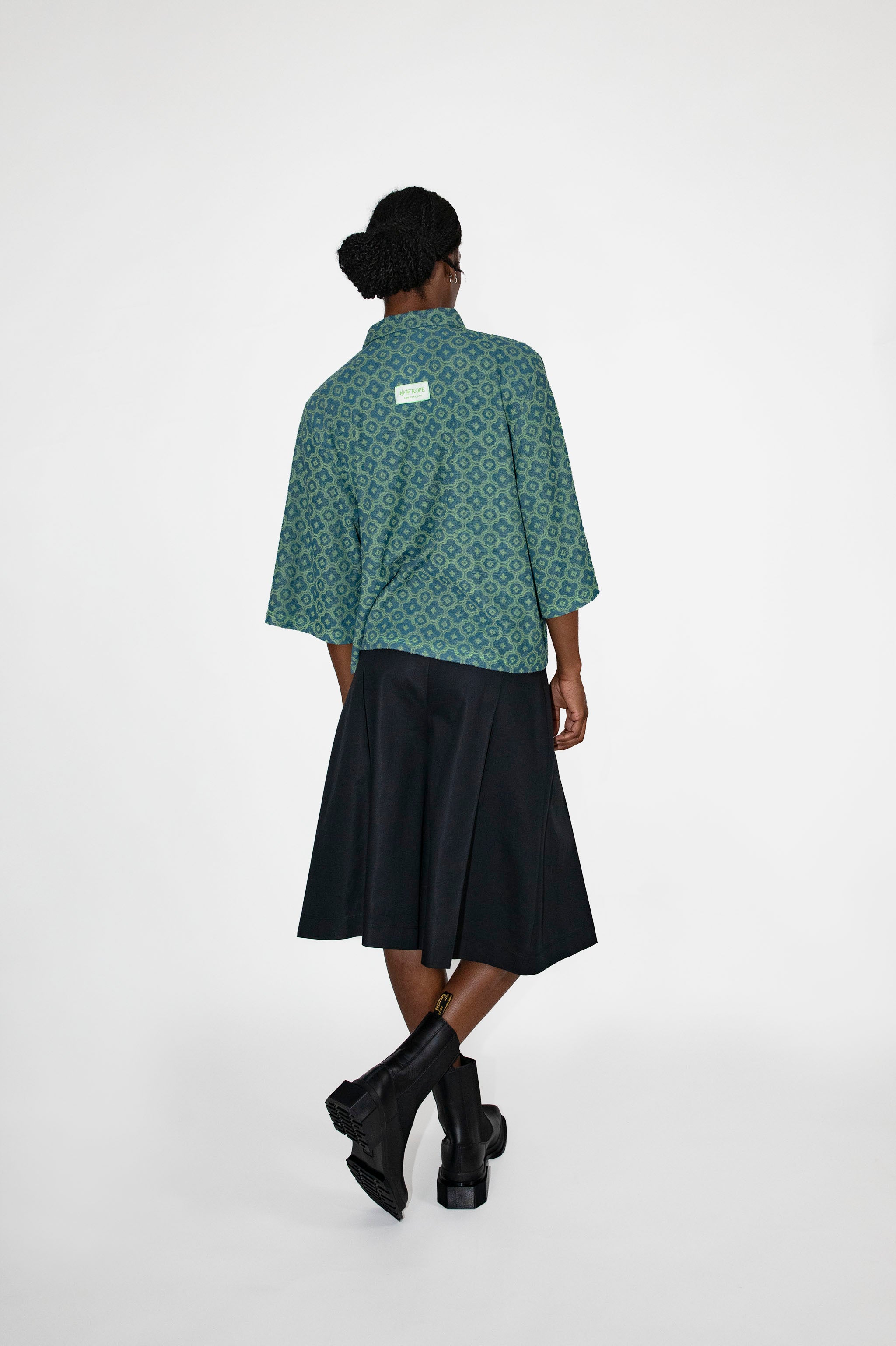 Person wearing a green patterned polo shirt and black skort on a white background