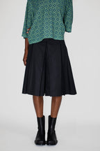 Person wearing a green patterned polo shirt and black skort on a white background